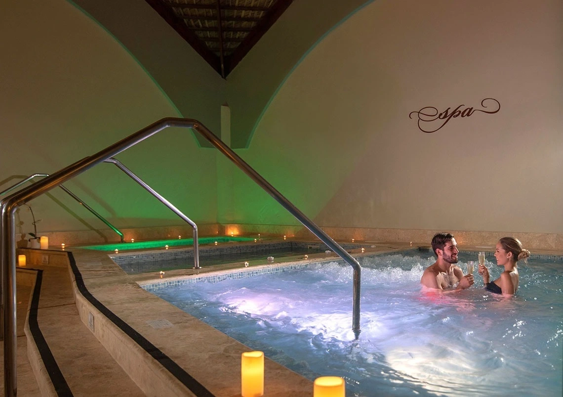 Pareja brindando en el jacuzzi del spa iluminado con velas
