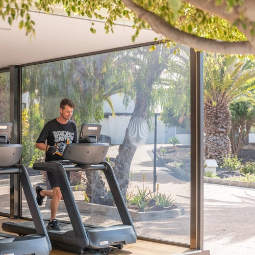 Pareja corriendo en cintas en un gimnasio acristalado con vistas al jardín