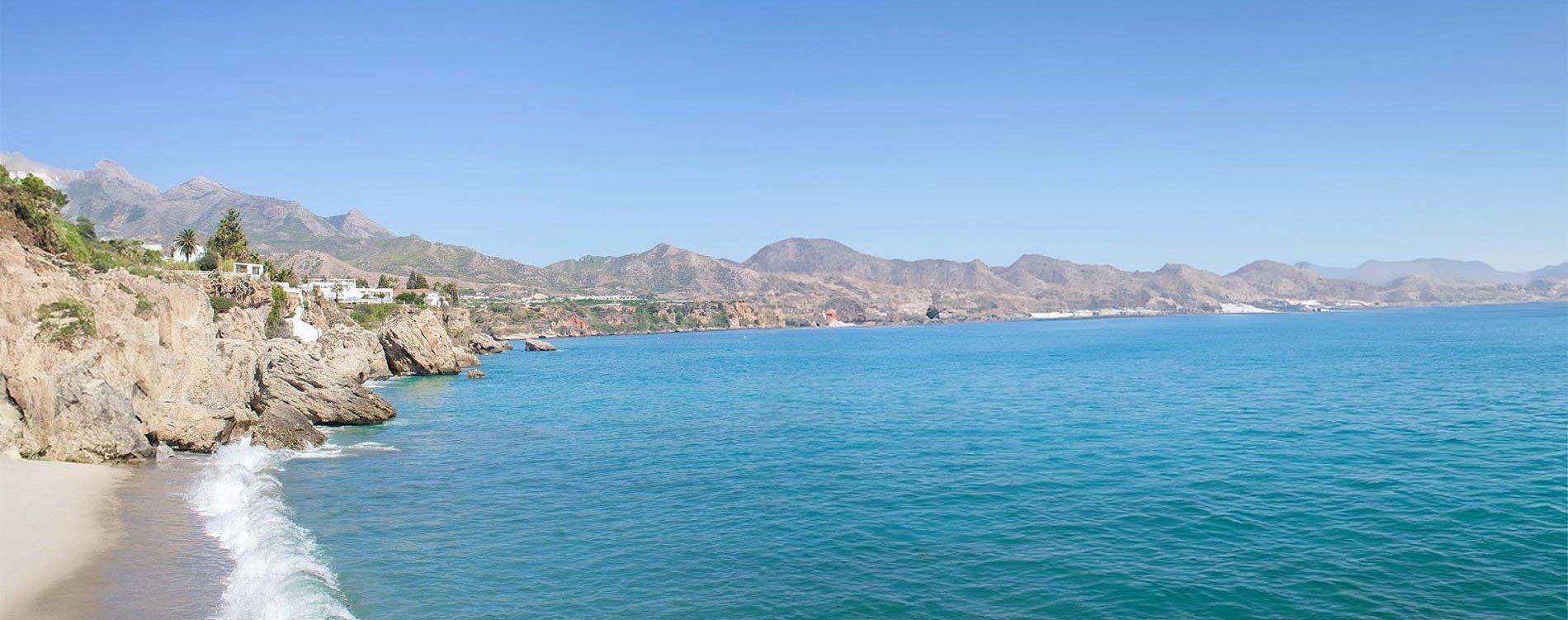 un océano con montañas en el fondo y una playa en primer plano