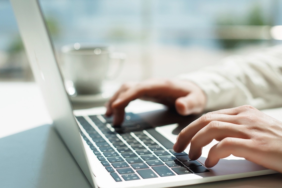 Hands typing on a laptop in a bright hotel workspace with a coffee cup.
