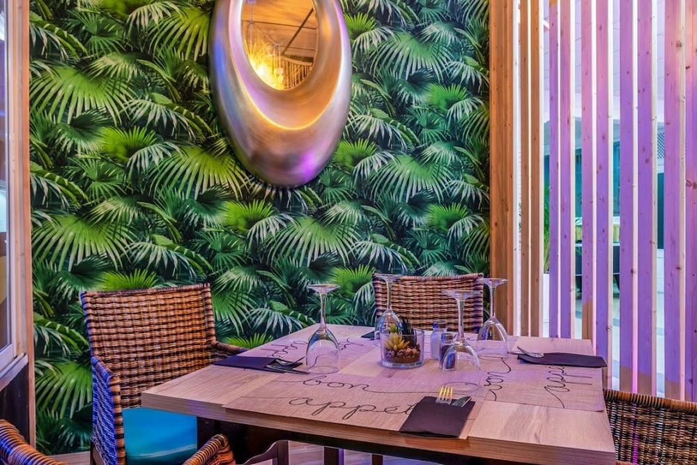 Restaurante de hotel con diseño tropical, sillas de mimbre, mesa de comedor y detalles modernos.