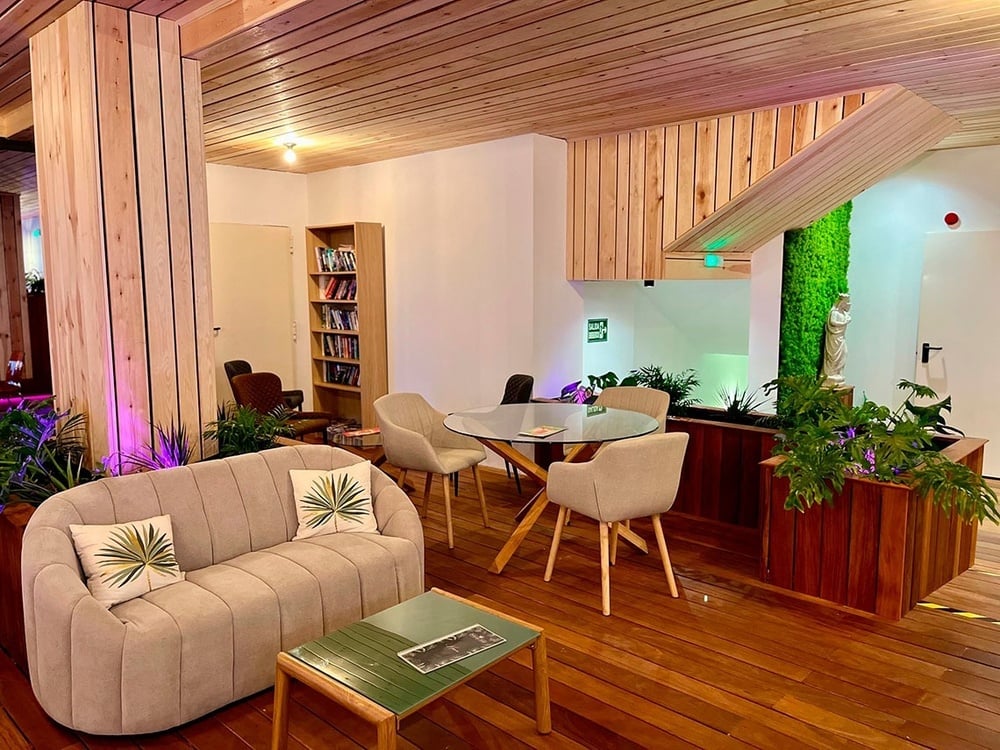 Lobby de hotel moderno y acogedor con sofás, mesas de madera y abundante vegetación.