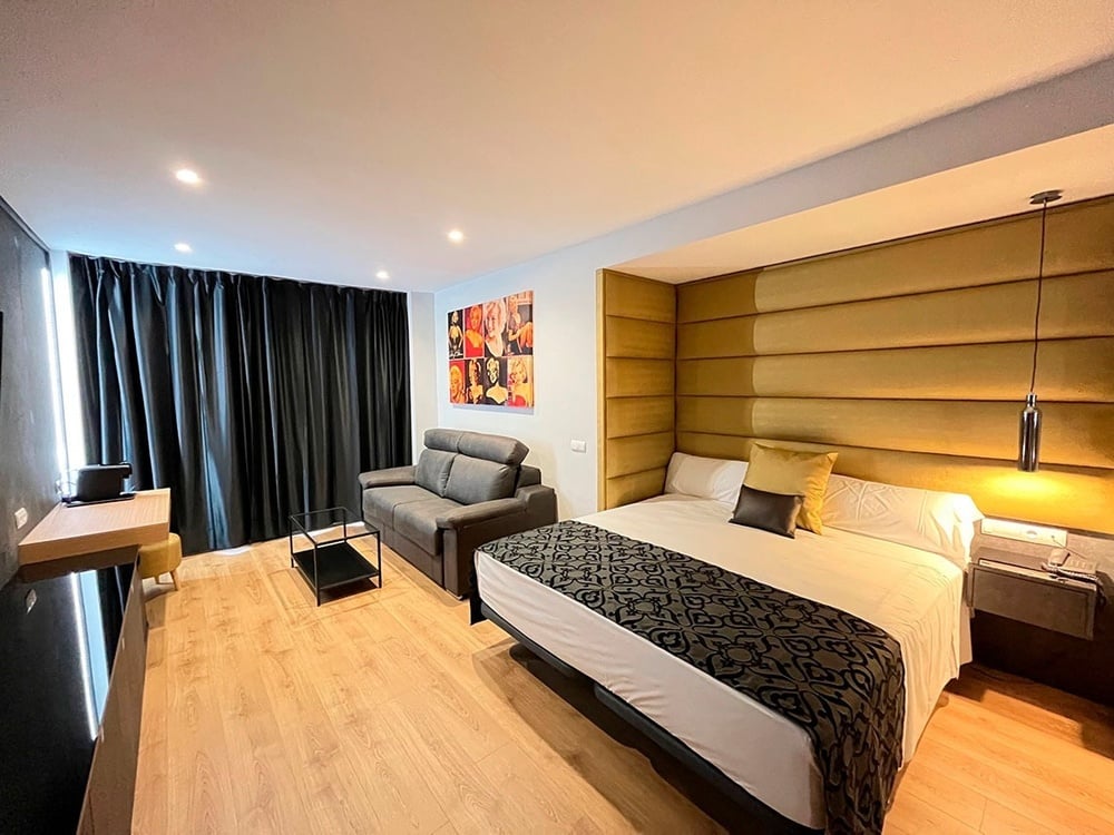 Espaciosa habitación de hotel moderna con cama grande, sofá, escritorio y decoración vibrante.