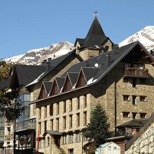 un grand bâtiment en pierre avec un toit en ardoise et des voitures garées devant