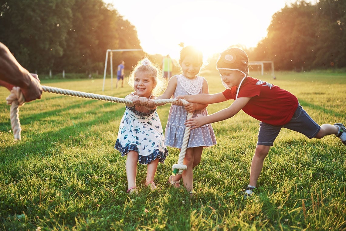 a boy and two girls are pulling a rope in a field