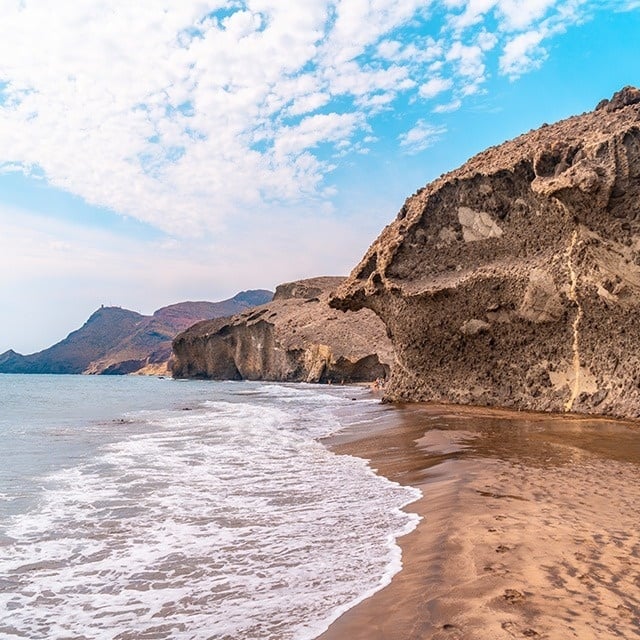 waves crashing on a sandy beach with mountains in the background