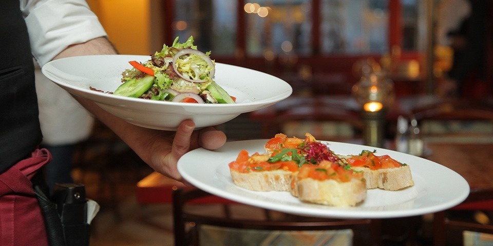 un camarero lleva dos platos de comida en un restaurante