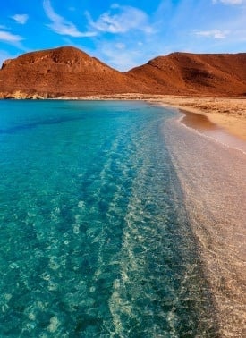 a beach with mountains in the background and a clear blue ocean .