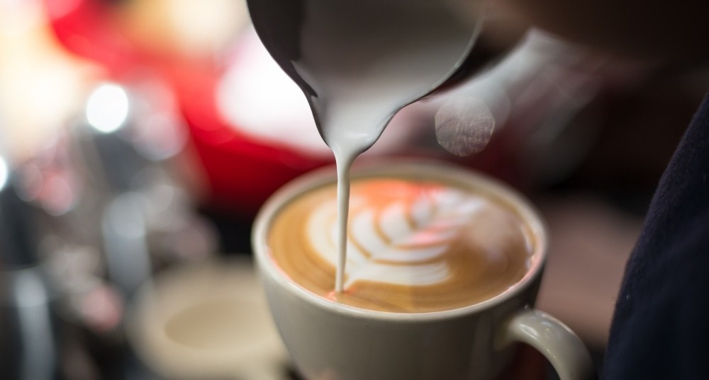 una persona está vertiendo leche en una taza de café