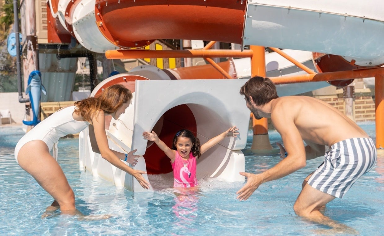 un hombre y una mujer ayudan a una niña a salir de un tobogán en una piscina