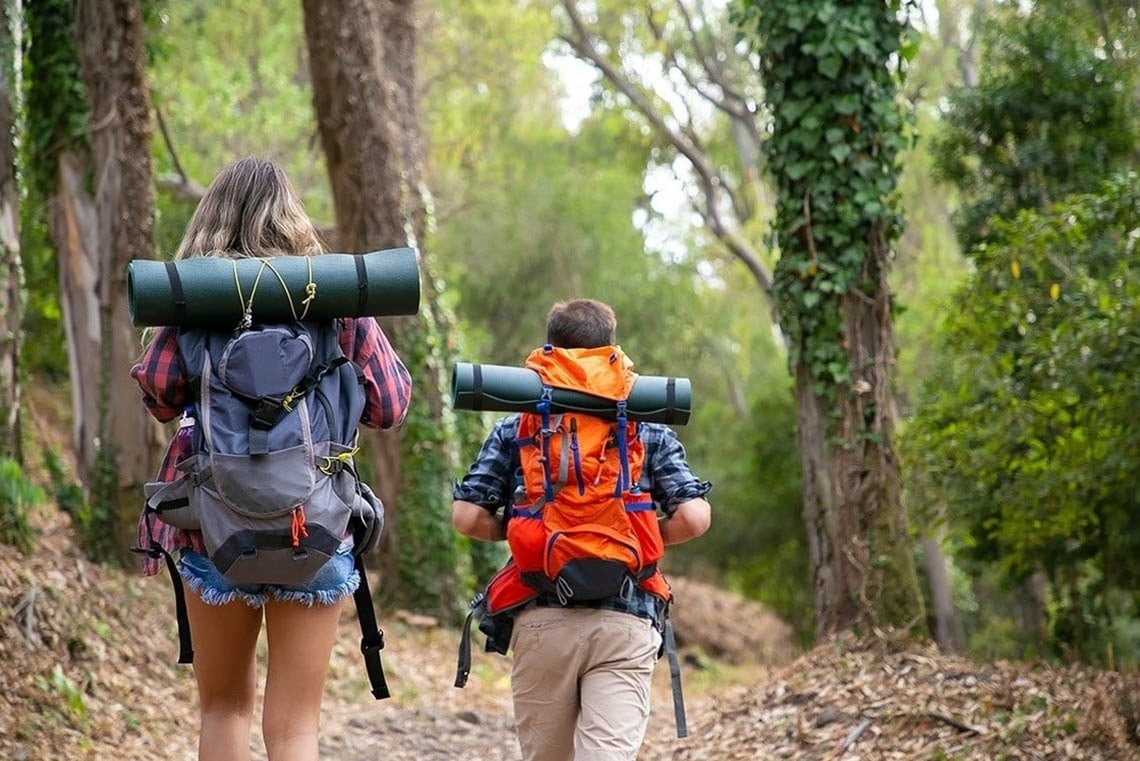 un hombre y una mujer con mochilas caminan por un sendero forestal