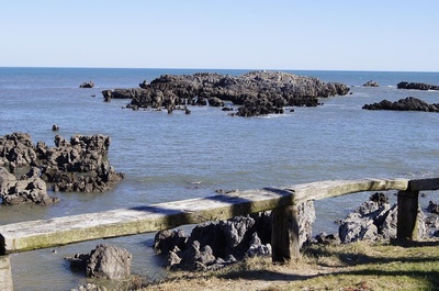 un banco de madera junto a un océano con rocas en el primer plano - 