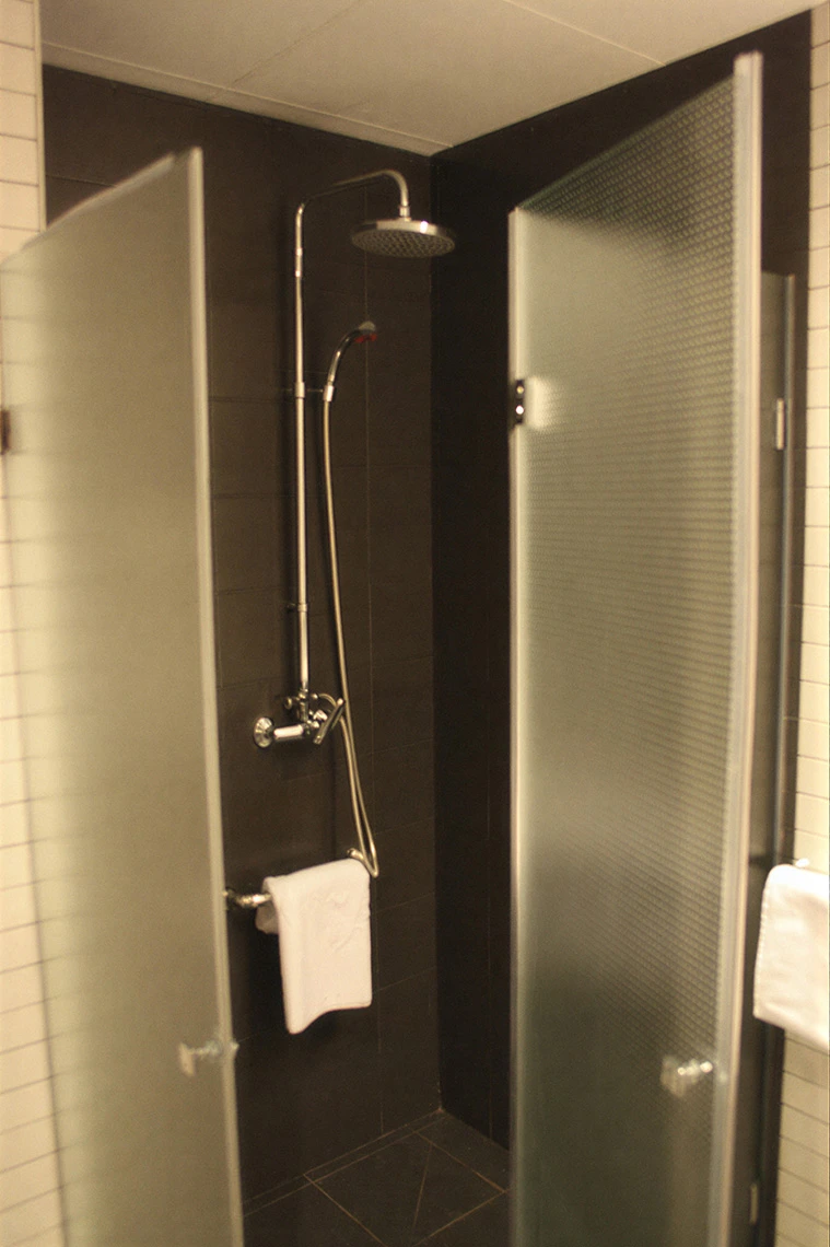 Ducha moderna con puerta de cristal esmerilado y toalla blanca, perfecta para tu Hotel Acosta Ciudad de la Música.