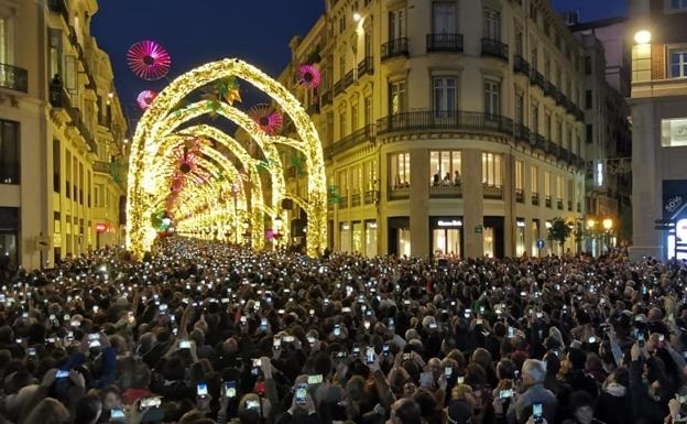 una gran multitud de personas está tomando fotos de las luces de navidad