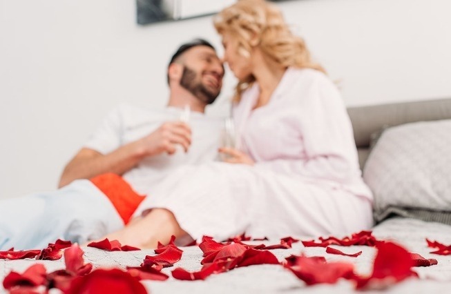 um homem e uma mulher estão sentados em uma cama cercada por pétalas de rosas .