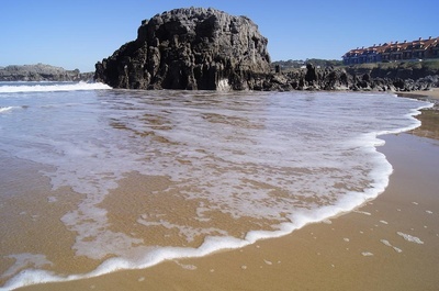 waves crashing on a sandy beach with a large rock in the background - 