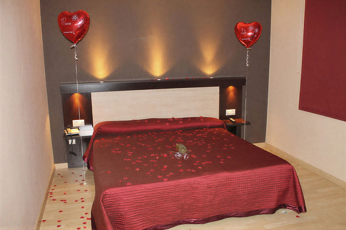 Habitación romántica con pétalos de rosa, globos de corazón y Hotel Acosta Ciudad de la Música.