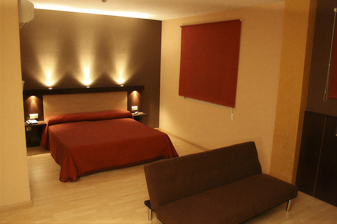 Habitación de hotel con cama matrimonial Hotel Acosta Ciudad de la Música, sofá y decoración moderna.