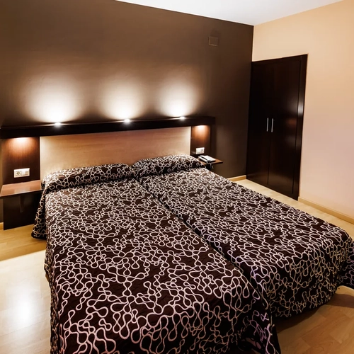 Modern hotel room with two beds, dark brown bedding, and ambient lighting. Hotel Acosta Ciudad de la Música.