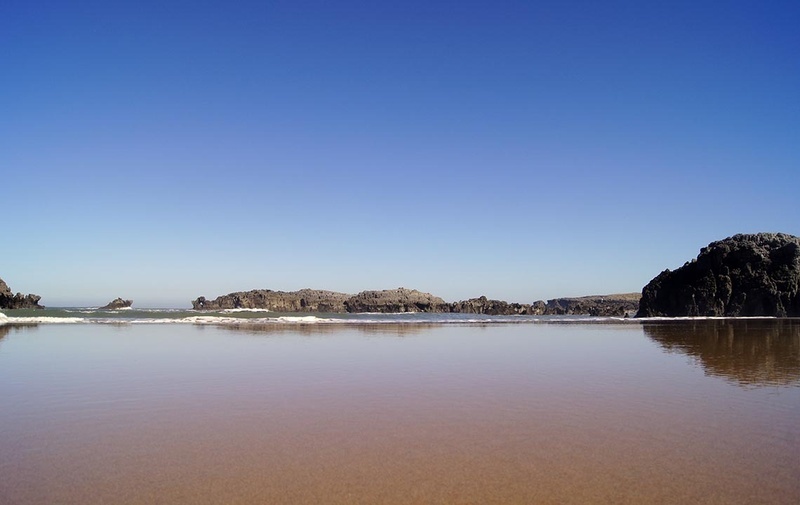 a beach with rocks in the background and a blue sky