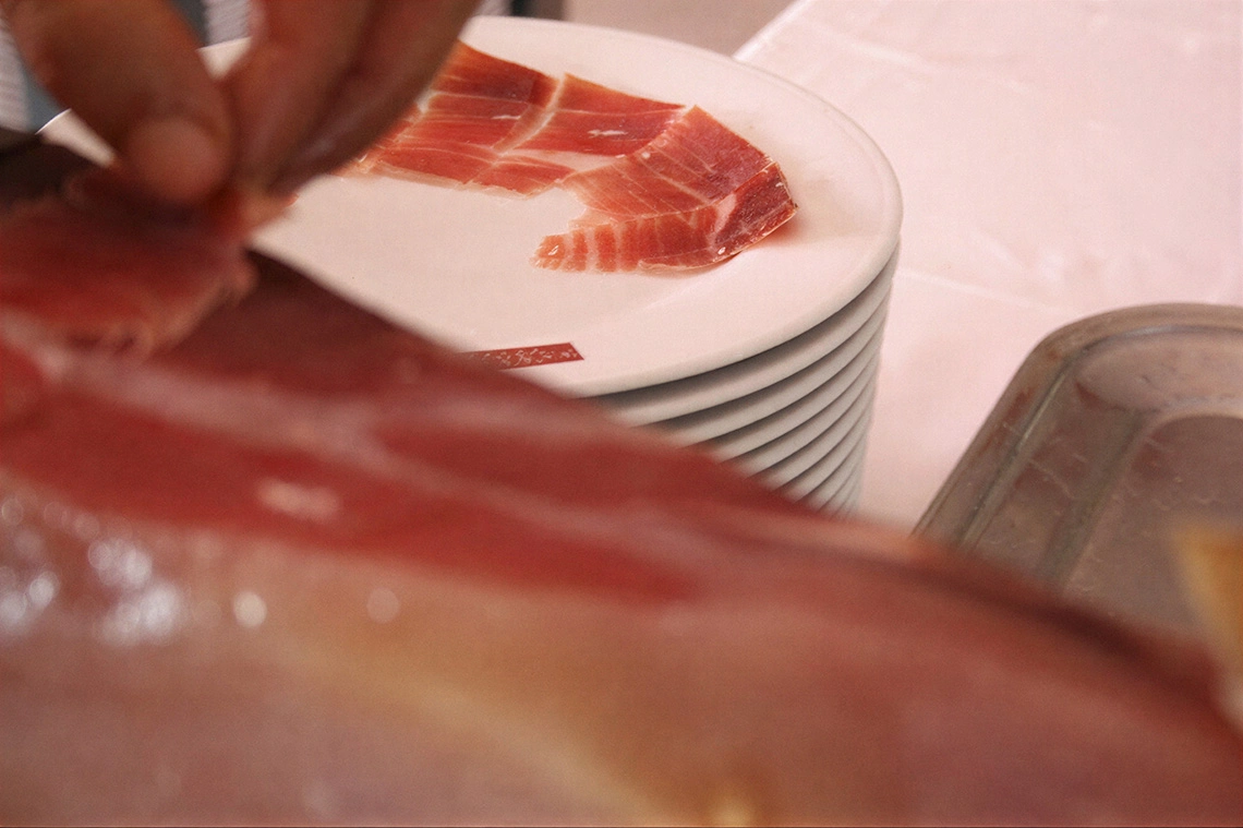 Mano cortando y sirviendo jamón. Exquisita experiencia culinaria en Acosta: Ciudad de la Música.
