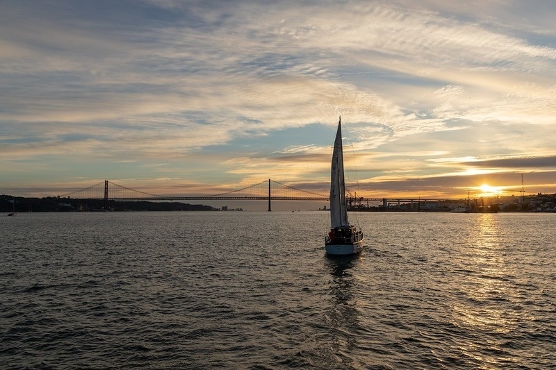 un velero en el océano al atardecer con un puente en el fondo