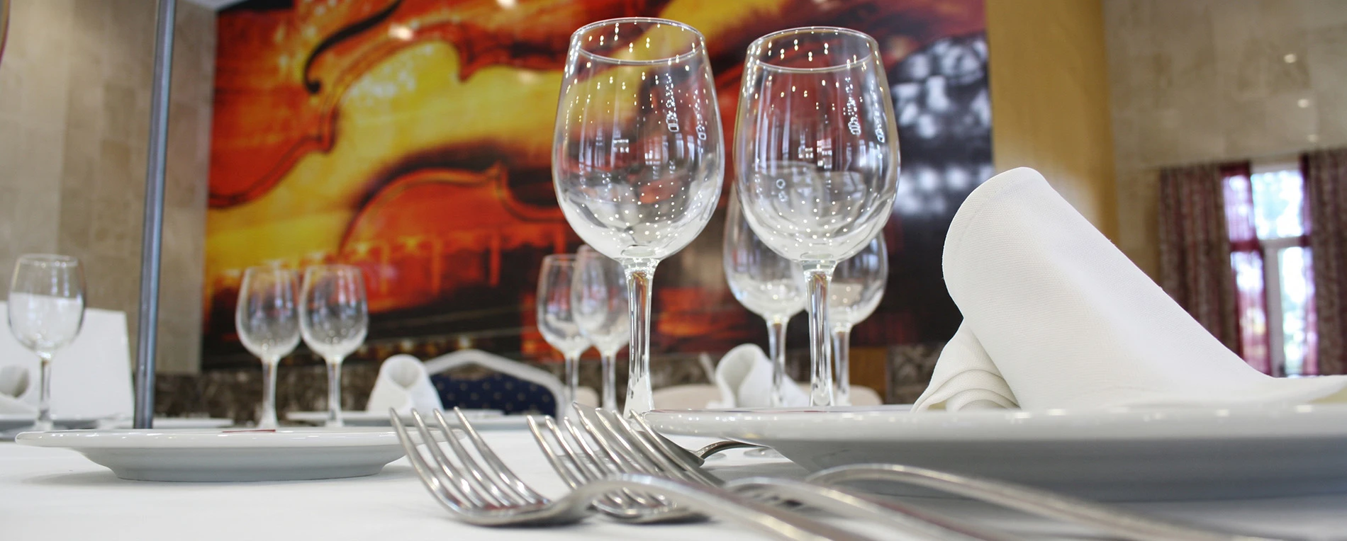 Mesa de hotel con copas y cubiertos. Fondo con arte musical Acosta: Ciudad de la Musica.