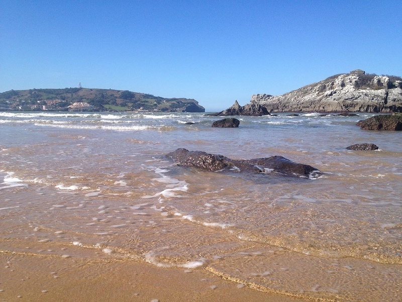 a beach with rocks in the water and a mountain in the background