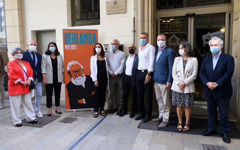 un grupo de personas con máscaras de pie frente a un cartel que dice berlanda