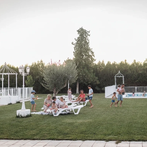 Families enjoy a poolside lounge area at the Hotel Acosta Ciudad de la Música, with lush green grass and trees.