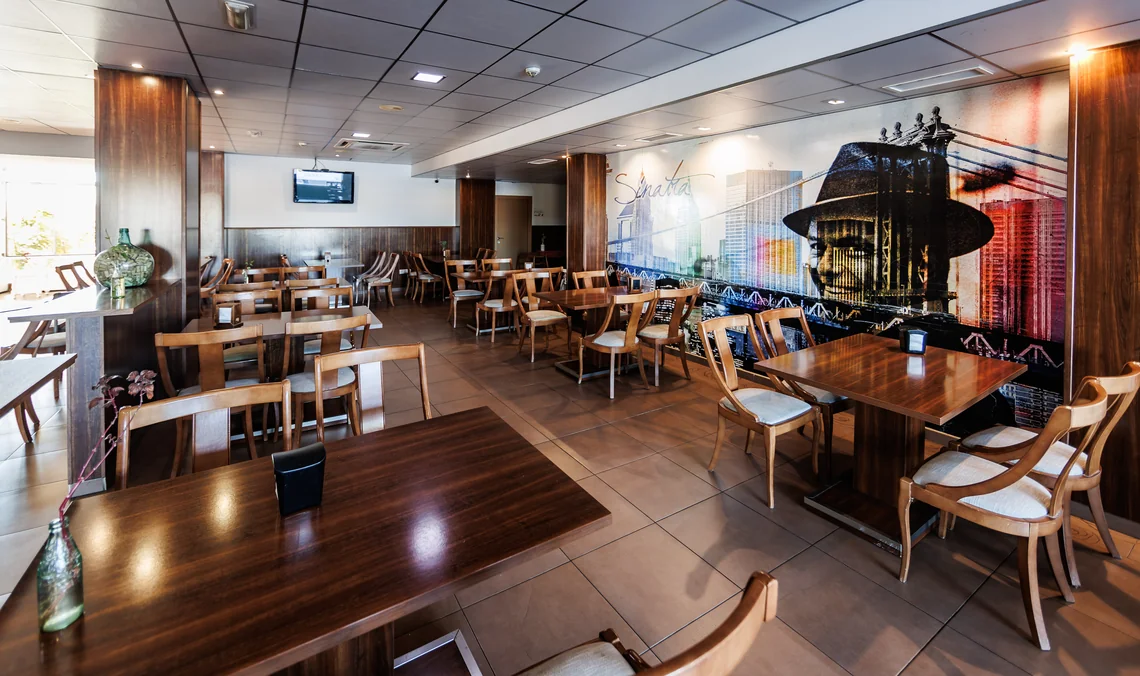 Interior de restaurante: mesas de madera, sillas y un mural de Frank Sinatra en un hotel. Hotel Acosta Ciudad de la Música