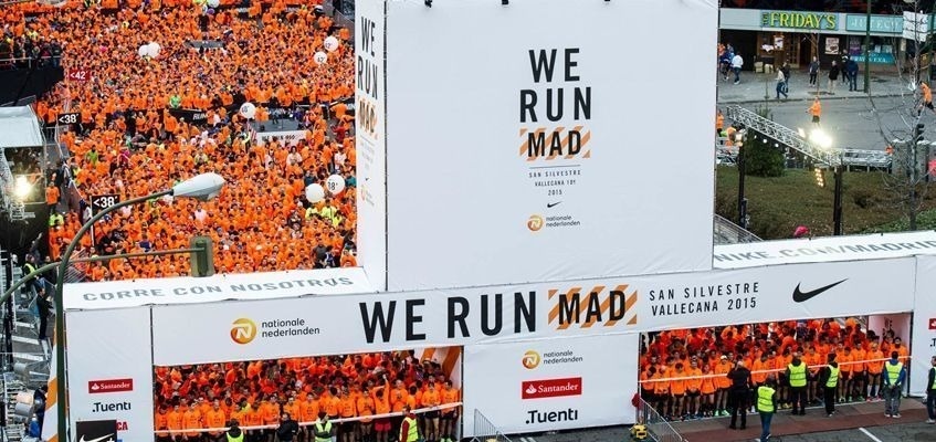 une foule de personnes vêtues de chemises orange se tient à côté d' un grand panneau qui dit we run mad