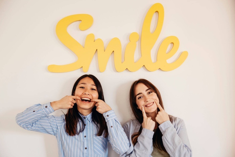 duas mulheres fazem caretas em frente a uma placa amarela que diz smile