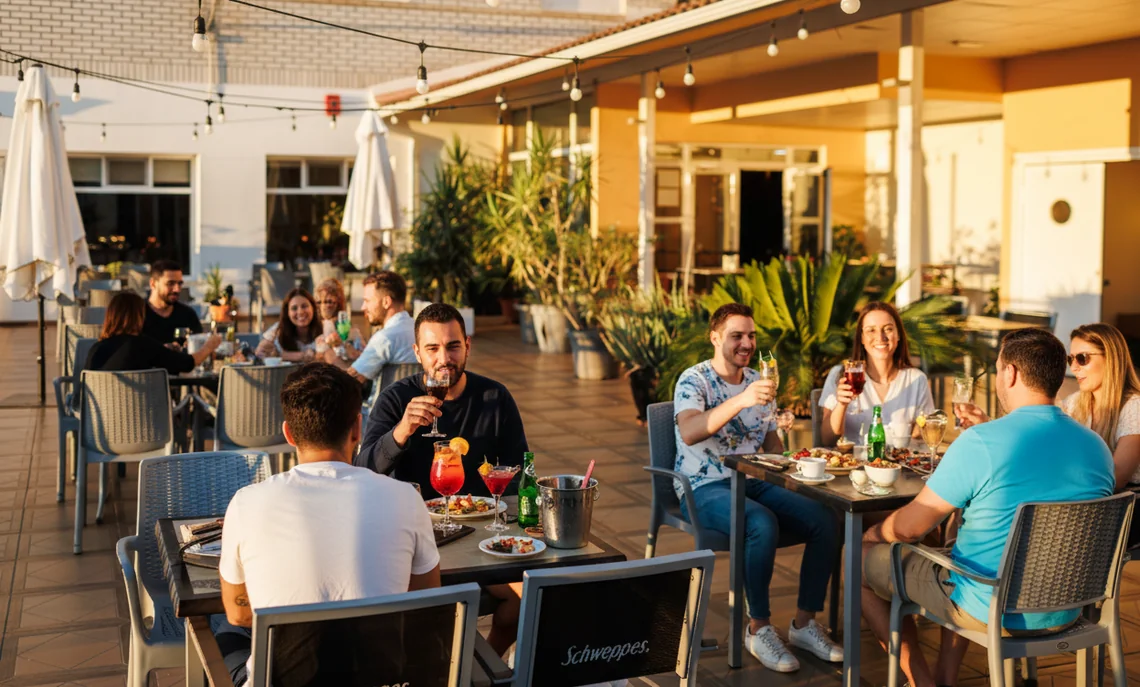 Terraza de hotel con gente disfrutando de bebidas Hotel Acosta Ciudad de la Música al atardecer.