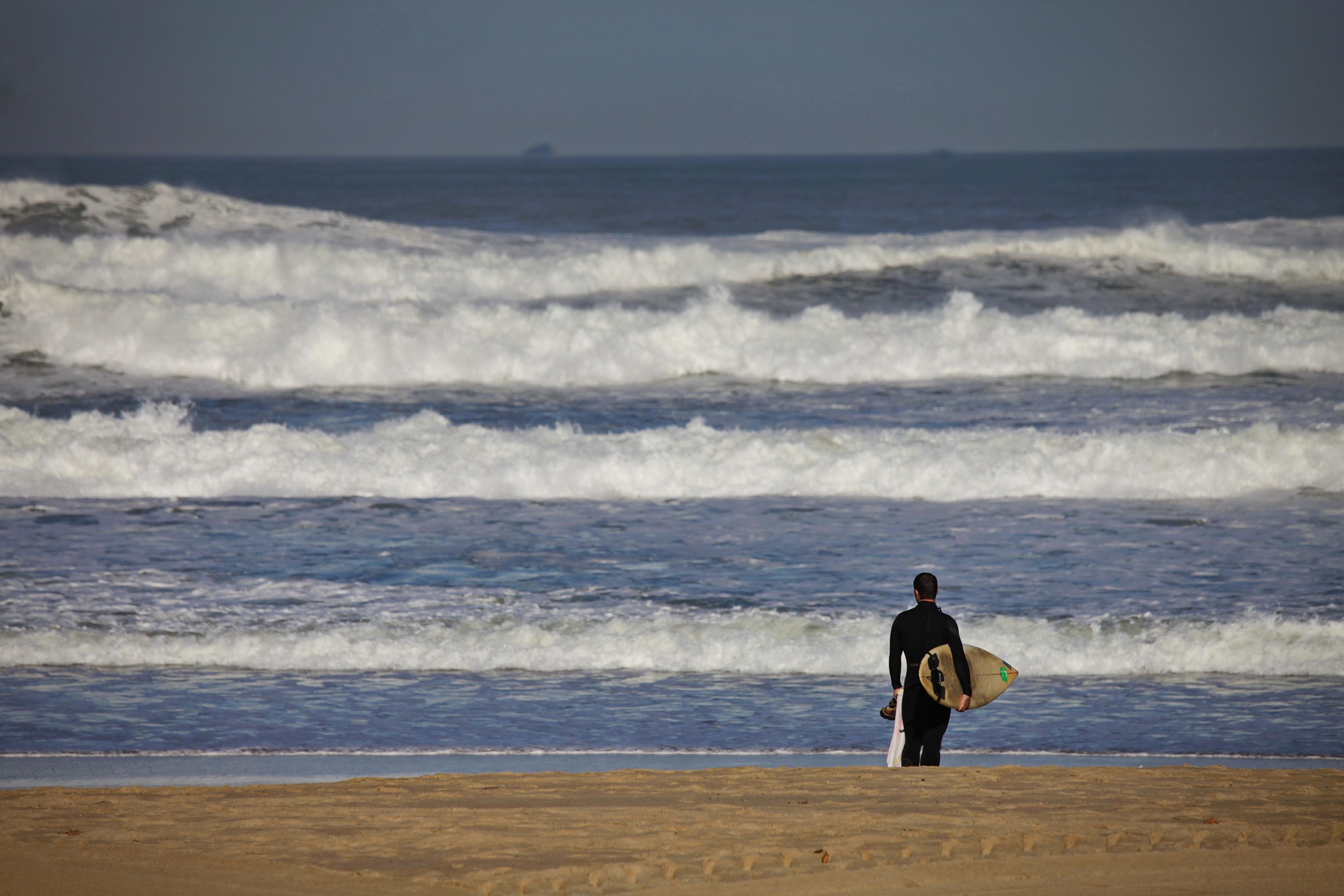 un hombre sostiene una tabla de surf mientras camina por la playa