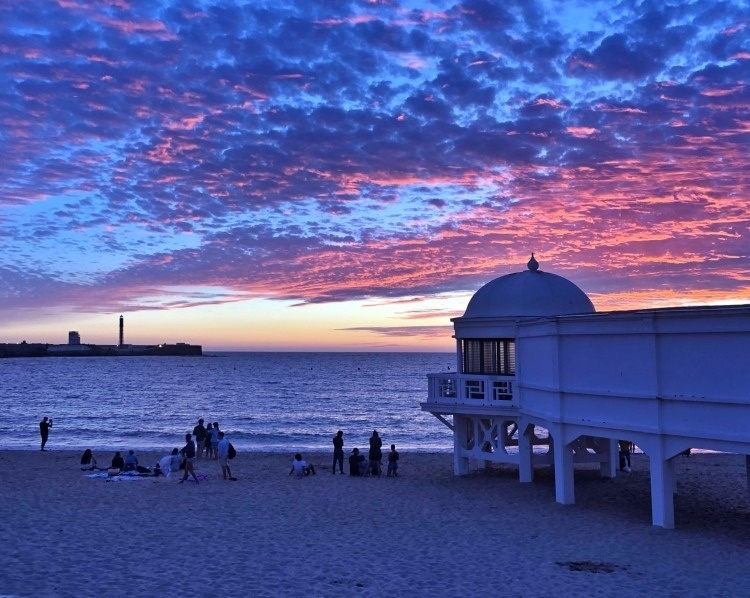 un grupo de personas se reúnen en la playa al atardecer