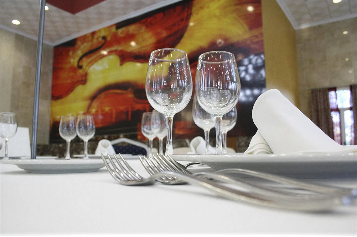 Mesa de restaurante en Acosta: Ciudad de la Musica, con copas de vino y mural musical.