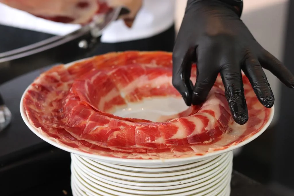 Mano cortando y sirviendo jamón. Exquisita experiencia culinaria en Acosta: Ciudad de la Música.