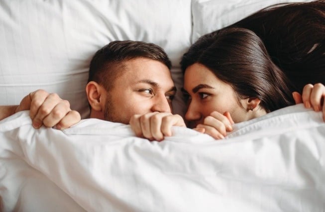 a man and a woman are laying under a blanket and looking at each other