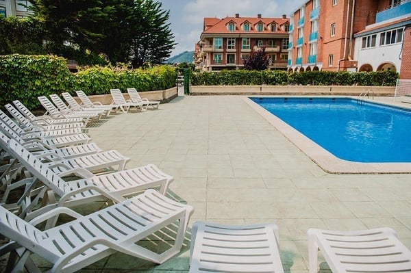 a large swimming pool surrounded by white chairs with a brick building in the background