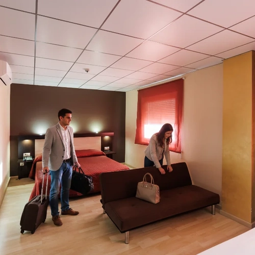 Modern hotel room with a man and suitcase, sofa bed, and a woman Hotel Acosta Ciudad de la Música.