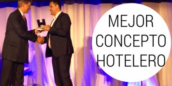 dos hombres se dan la mano en un escenario con la palabra mejor concepto hotelero en el fondo