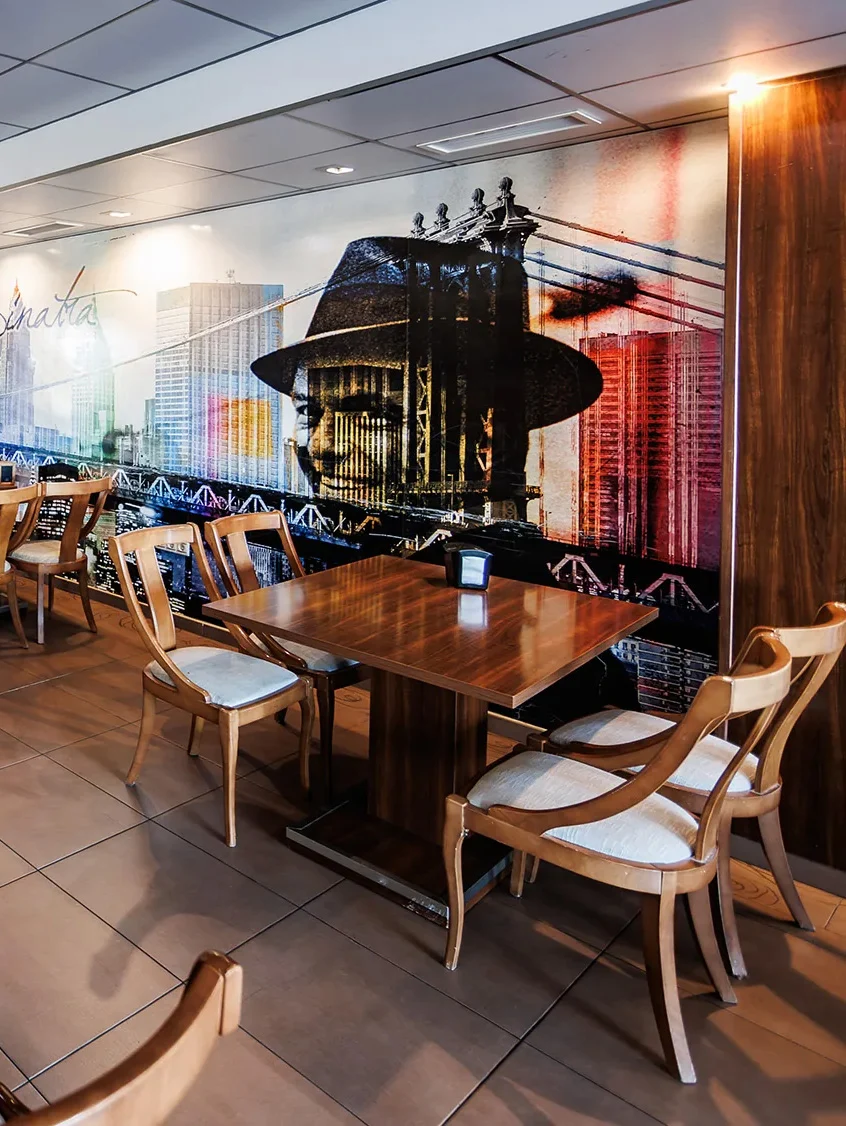 Interior de restaurante: mesas de madera, sillas y un mural de Frank Sinatra en un hotel. Hotel Acosta Ciudad de la Música