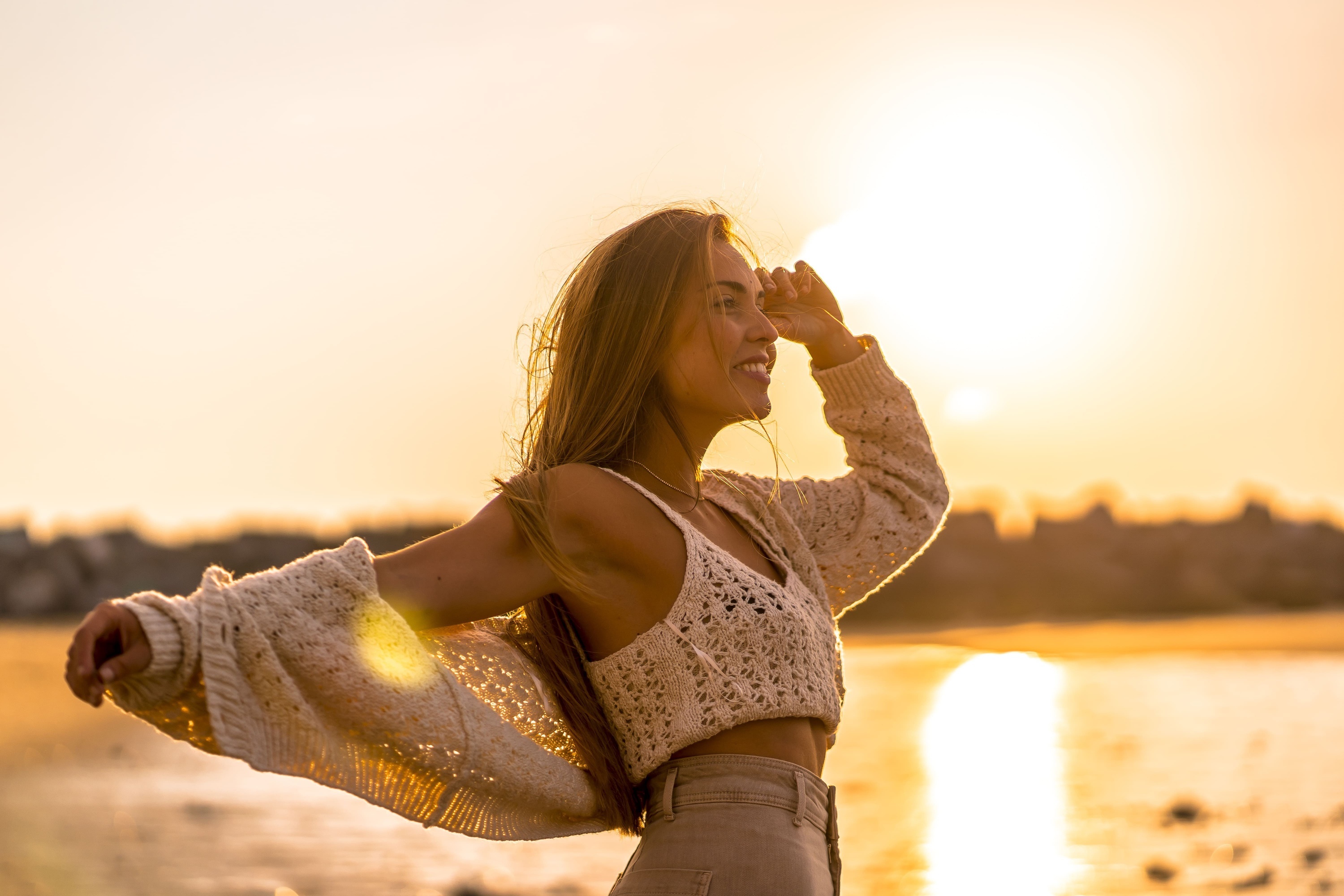 una mujer con los brazos abiertos se para en la playa al atardecer
