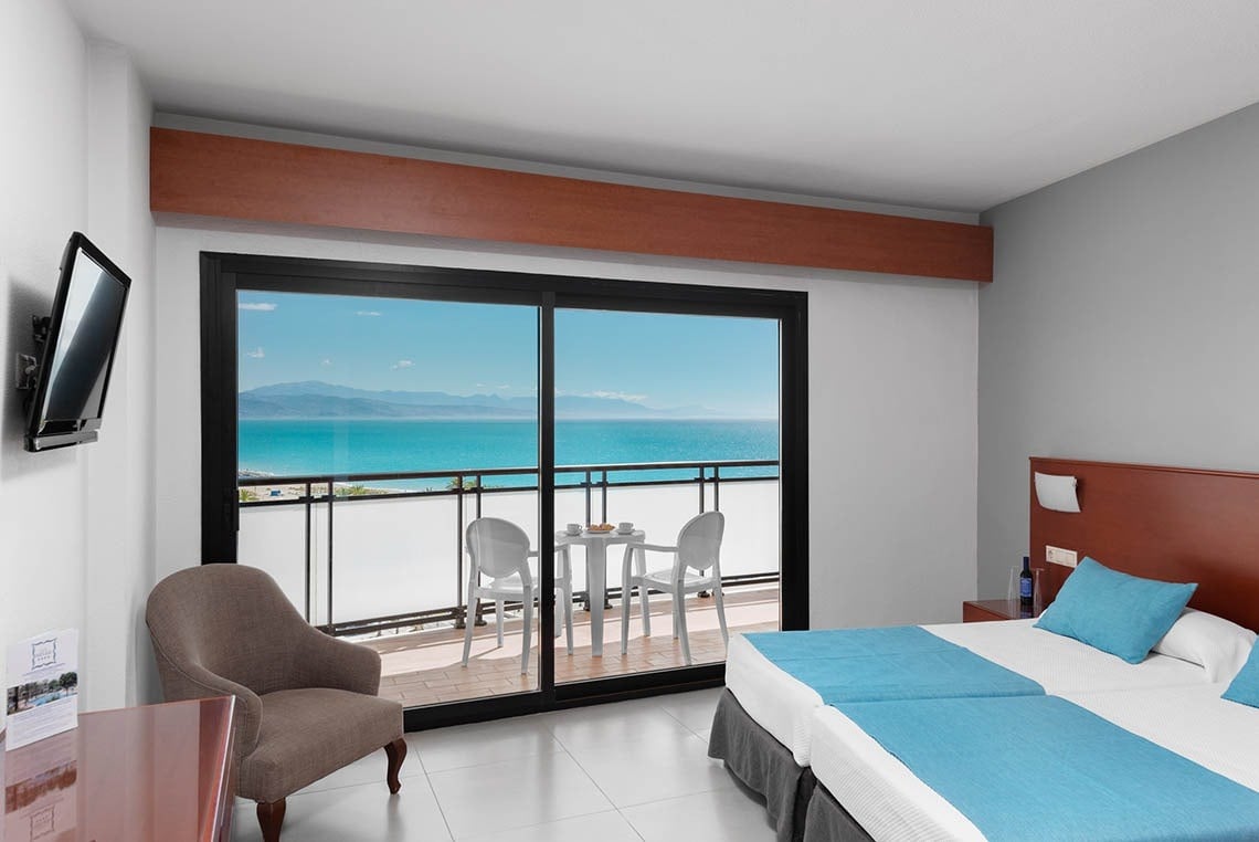 a hotel room with two beds and a balcony overlooking the ocean