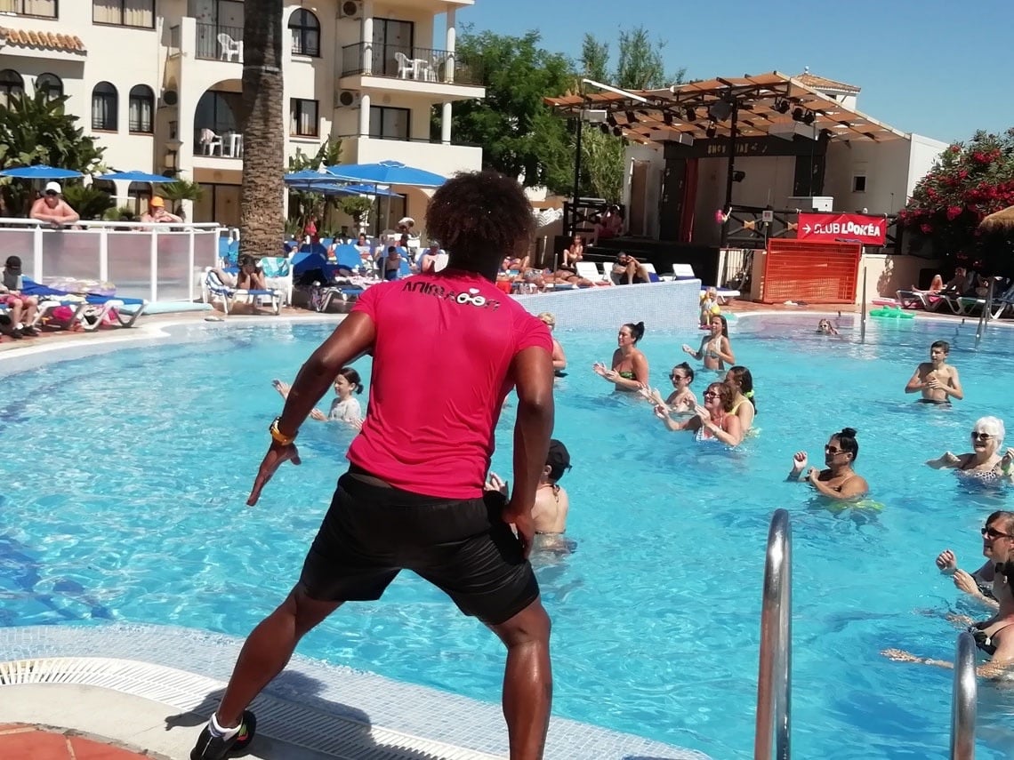 une femme vêtue d' un t-shirt rose et d' un short noir se tient devant une piscine remplie de personnes