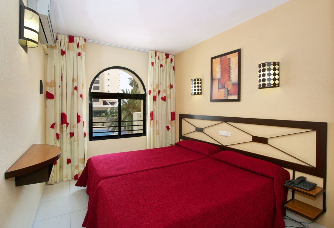 una habitación con dos camas y una ventana con cortinas rojas