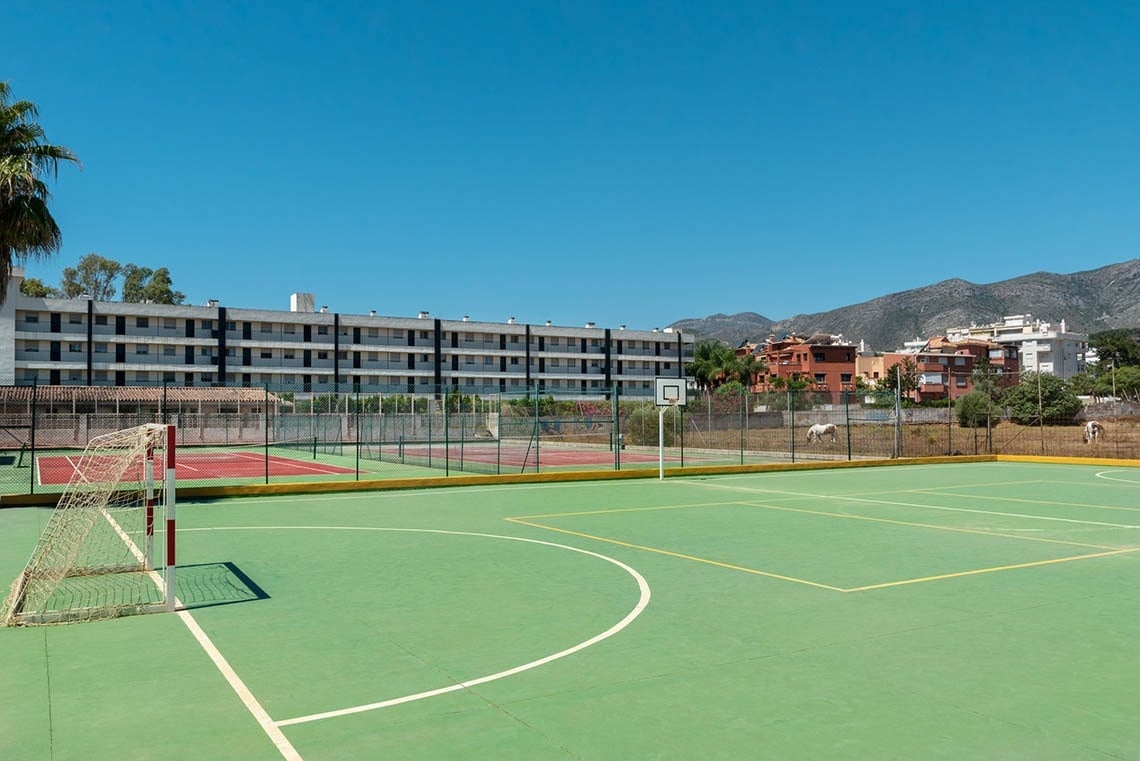 a basketball court with a fence around it and a building in the background