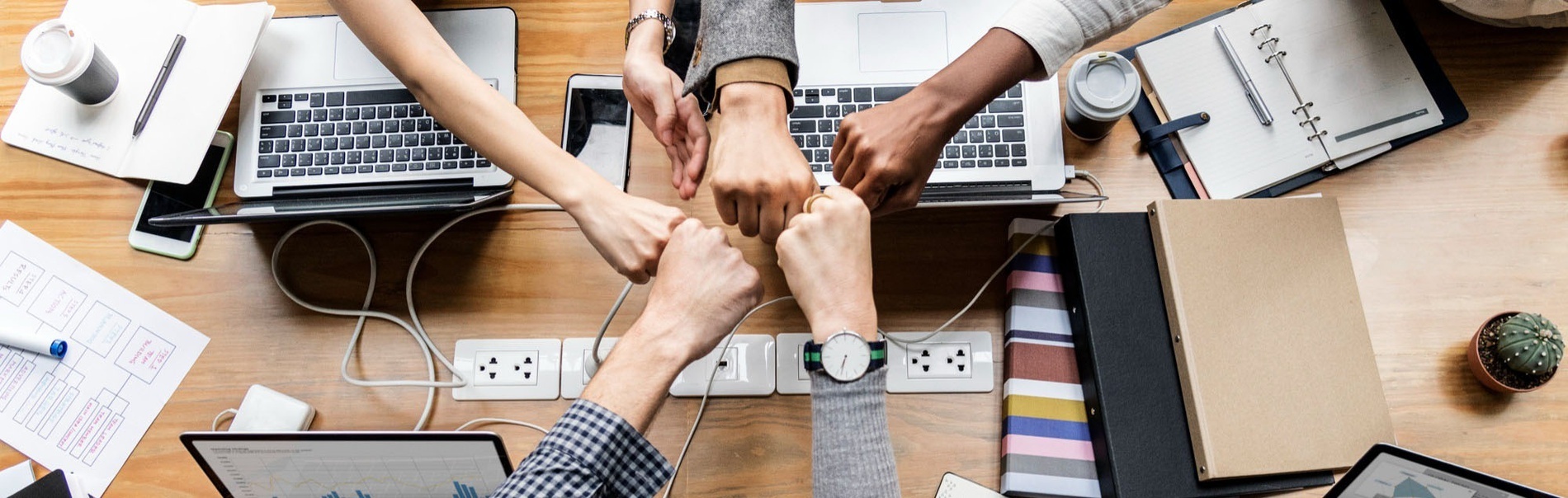 a group of people putting their hands together in front of laptops