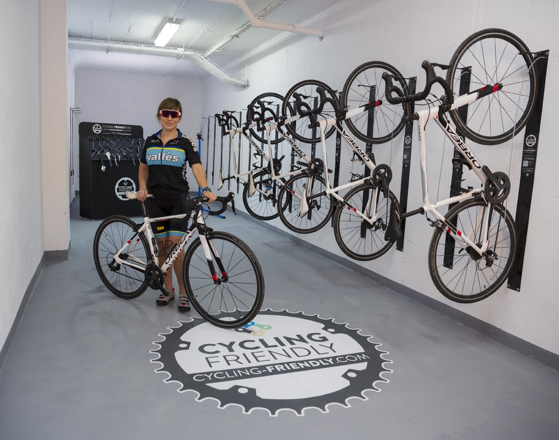 une femme se tient à côté d' un vélo dans une pièce avec un vélo suspendu au mur